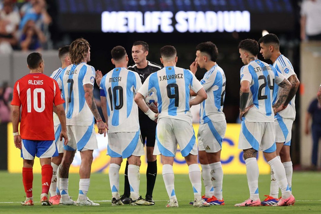 El árbitro uruguayo Andrés Matonte (c) fue registrado este martes, 25 de junio, al hablar con jugadores de la Albiceleste al esperar la decisión del VAR que validó el gol que el argentino Lautaron Martínez le anotó a Chile, durante un partido de la fecha 2 del grupo A de la Copa América, en el estadio MetLife de East Rutherford (Nueva Jersey, EE.UU.). EFE/Justin Lane