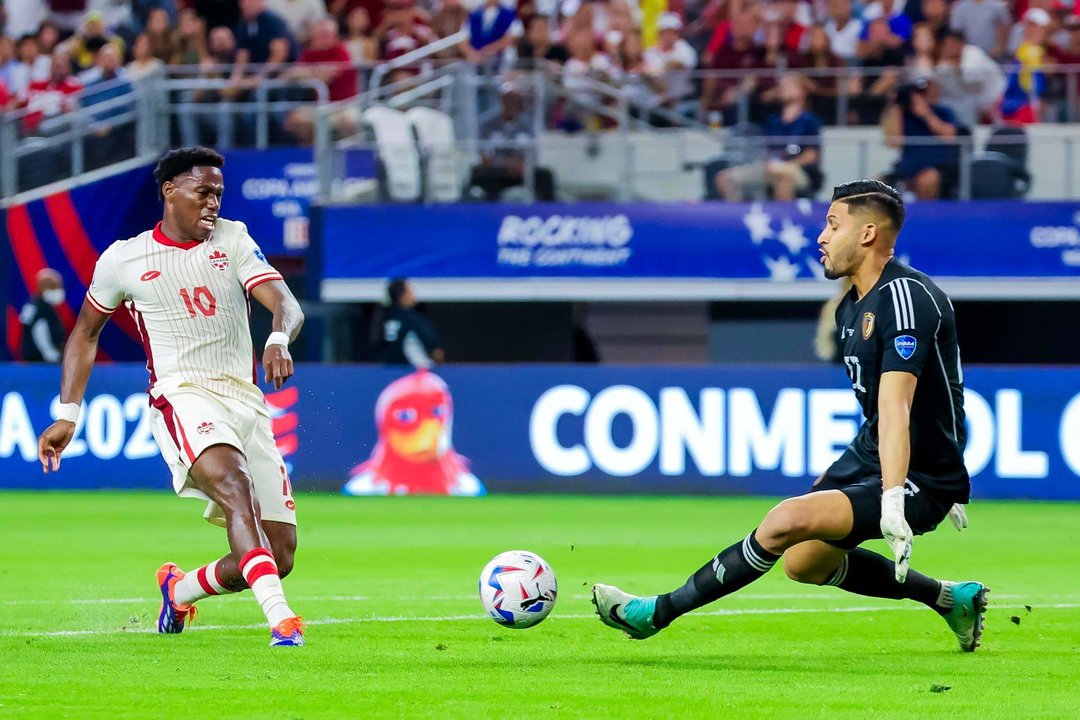 El guardameta de Venezuela, Rafael Romo (d), fue registrado este viernes, 5 de julio, al intentar bloquearle un balón disparado por el delantero canadiense Jonathan David (i), durante el segundo partido de los cuartos de final de la Copa América 2024, en el estadio AT&T de Arlington (Texas, EE.UU.). EFE/Kevin Jairaj